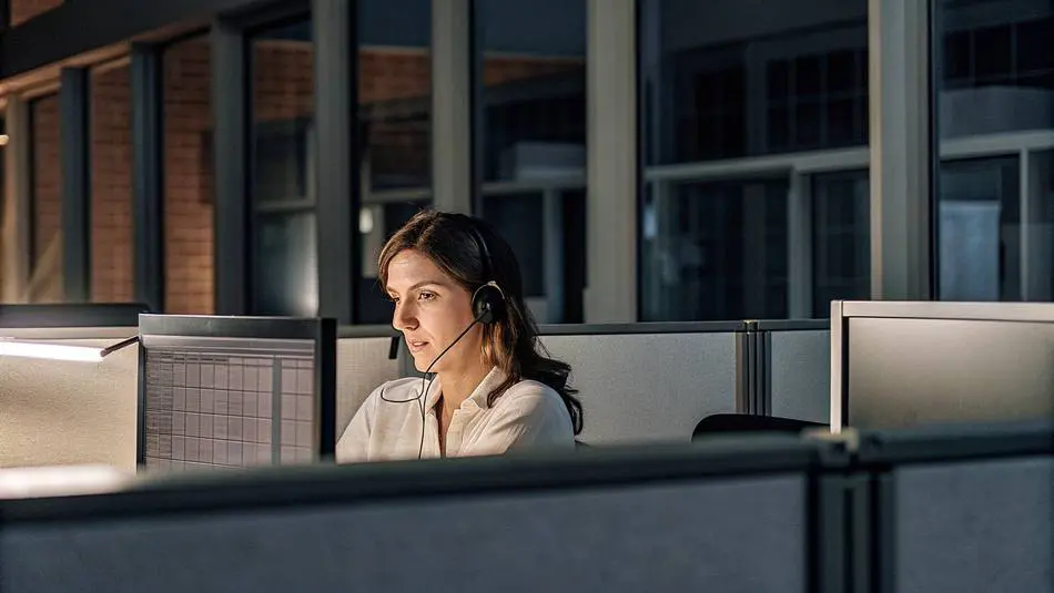 A woman wearing a headset working at a computer in an office at night