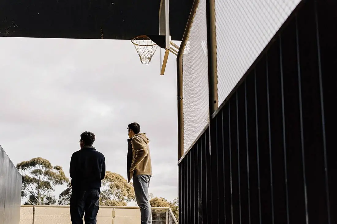 Two young men standing under a basketball hoop at an outdoor court