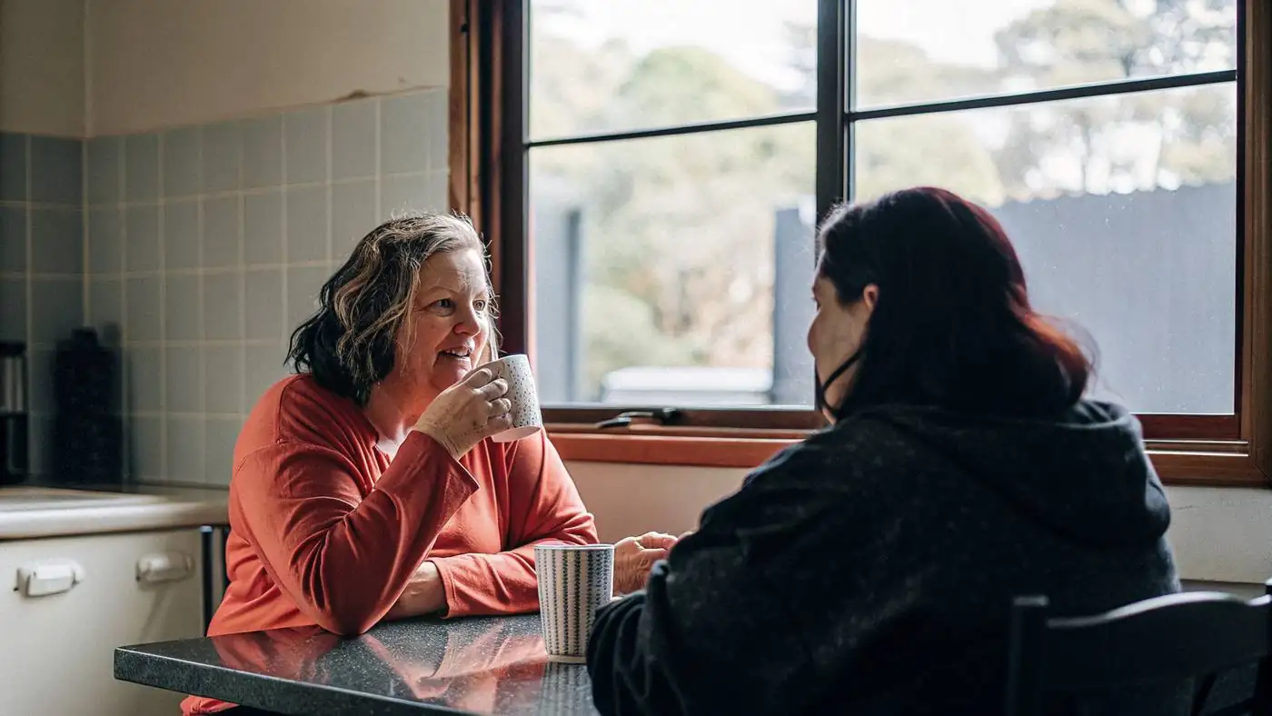 Two women talking over cups of tea at a kitchen table